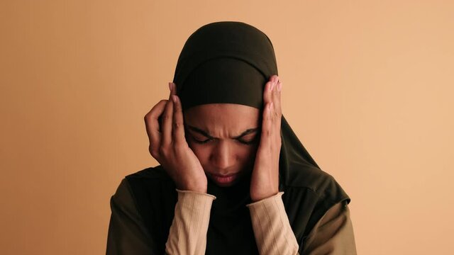 A sad arabian woman is grabbing her head standing isolated over beige background