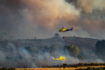 Two helicopters, bambi bucket and firefighters in the background