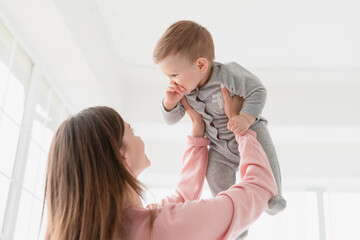 Happy young mother lifting playing with her little small son daughter infant newborn baby, giving...