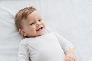 Cute little small child caucasian infant toddler newborn smiling with baby milk teeth lying on the comfortable bed. Teething concept, childcare and parenthood. Copy space