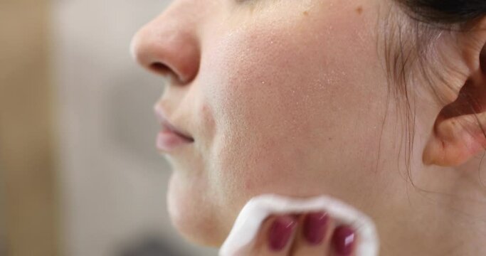 Woman is removing makeup from her face cleaning facial skin, portrait closeup.Girl is wiping face skin looking at camera