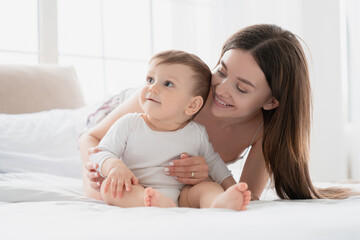 Family time. Happy young single mother having fun with son daughter infant newborn baby toddler playing on the bed together. Happy mother`s day! Maternity leave and motherhood