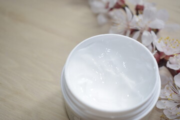 Moisturizing cream for face and body in a glass jar on a wooden surface with a blossoming sprig of apricots.