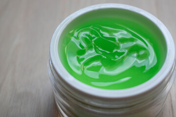 Aloe-based green face and body moisturizer in a glass jar on a wooden surface.