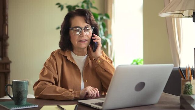 Woman talking on phone and using laptop at table in apartment room.