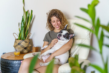 Woman dog lover with bulldog at home. Horizontal view of woman tickling dog isolated with plants.