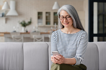 Fototapeta premium Beautiful middle-aged mature woman mother wife freelancer using smart phone for checking emails, social media, working online from home, e-shopping.