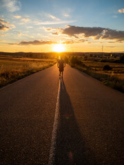 Strong man with his back turned on a road with the sun facing him at sunset. Summer sport image