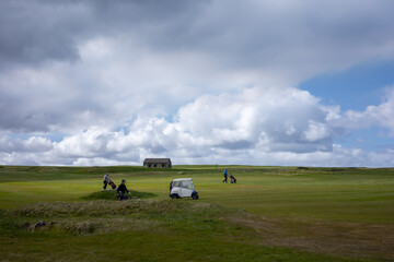 Golf players with wheel push carts, and riding an electric golf cart, on a green golf field, on...