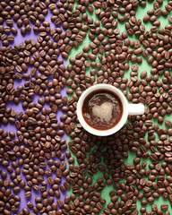 Espresso cup filled with coffee with coffee beans scattered around it on a green and purple background overhead shot