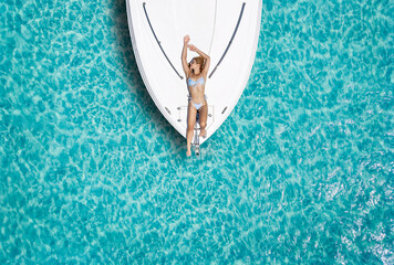 Top down view to a attractive woman in bikini taking a sunbath on a white luxury yacht over...