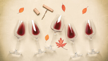 Flat lay red wine in glasses decorated with autumn leaves on a concrete beige background. Top view, wide.