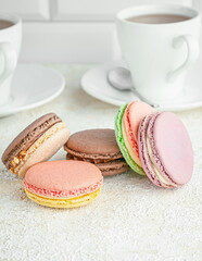 Macaroons are laid out on the table. In the background, cups with coffee. Close-up. Light background.