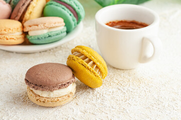Obraz premium Two macaroons are on the table. In the background, cups with coffee. And plate with macaroons. Close-up. Light background.