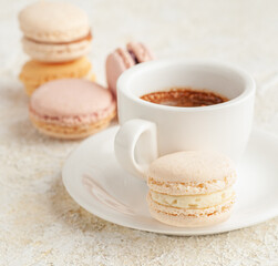 Macaroon is on a plate. In the background, cups with coffee. And macaroons laid out in a stack. Close-up. Light background.