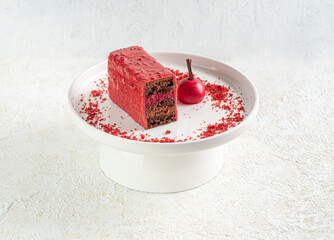 Chocolate covered cherry cake. Sponge cake with a layer of cherry jelly with chocolate mousse. Decorated with crumbs and chocolate. On a white plate. Light background.