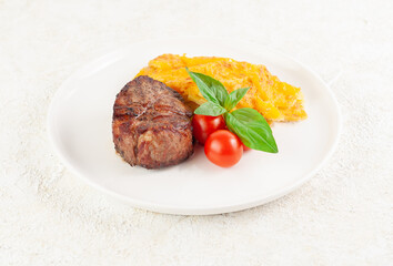 Filet mignon with baked potatoes, cheese, cherry tomatoes and basil on a white plate. Close-up. Light background.