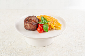 Filet mignon with baked potatoes, cheese, cherry tomatoes and basil on a white plate. Close-up. Light background.