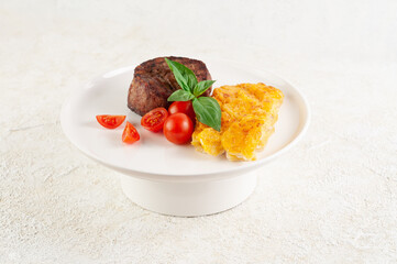 Filet mignon with baked potatoes, cheese, cherry tomatoes and basil on a white plate. Close-up....