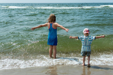 little girl and boy stand in the sea with outstretched arms