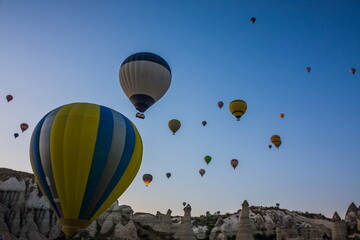 Fototapeta premium Hot air balloons flying over the valley at Cappadocia, Turkey. Goreme Balloon Festival. Beautiful hot air balloons take off at sunrise. Hot air balloons in the blue sky