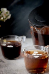 There is a teapot and two cups of black tea on the table