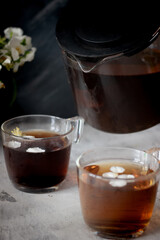 There is a teapot and two cups of black tea on the table