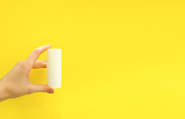 Female hand holding white cosmetic bottle on yellow background. Mock up, copy space. Summer skincare concept