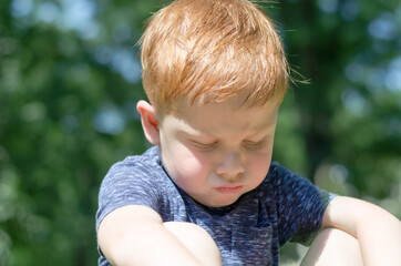 The child is offended. Portrait of a 4-year-old red-haired boy who sits in the sun and takes...