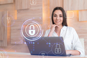 Attractive businesswoman in white shirt at workplace working with laptop to defend customer cyber security. Concept of clients information protection. Padlock hologram over office background.