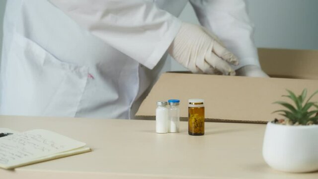 Doctor wearing medical mask and protective gloves packing drug medication delivery. Nurse putting medicine into box, pharmacist puts tablets and pills, closing parcel. Pharmacy shipping concept. 
