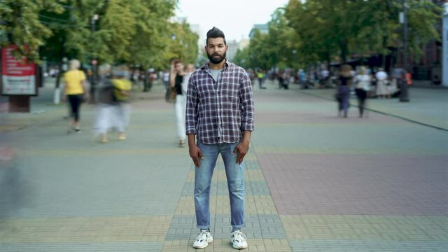 Time lapse portrait of attractive Arab man standing outside in crowded street looking at camera while girls and guys are walking around. Life and people concept.