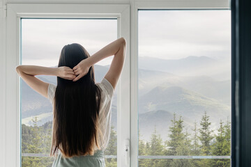 Young woman standing near window, hands above head - Powered by Adobe