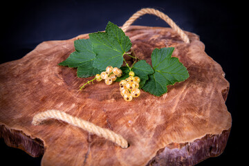 Weiße Johannisbeeren mit grünen Blättern auf ein Holzbrett angerichtet 