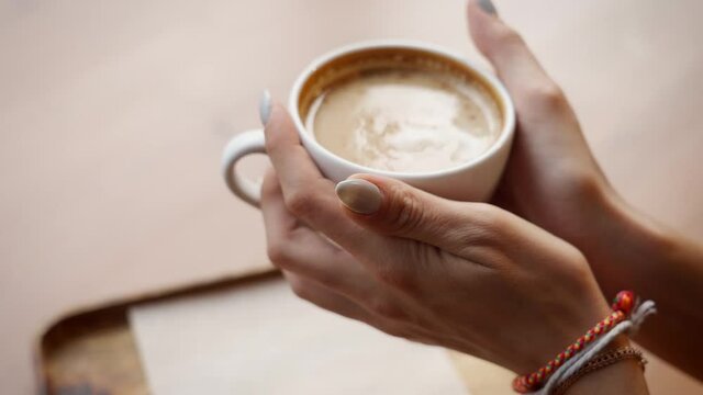 Female hands takes a cup of coffee. Woman warms her hands with hot coffee cup. Close up. 4K
