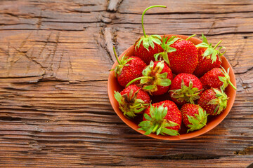 Ripe strawberries in a clay plate on a dark wooden surface.