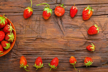 Ripe strawberries in a plate on a wooden table next to a frame.