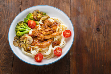 Udon with chicken in Japanese sauce and vegetables on a plate on a wooden table.