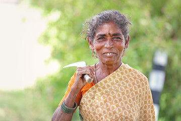 Indian Senior woman holding a sickle on farm field