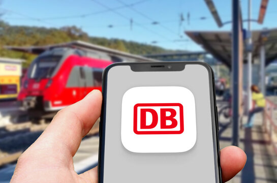DB Navigator Logo wird auf einem Smartphone angezeigt, dahinter ein einfahrender Zug im Bahnhof, App der Deutschen Bahn zur Auskunft von Fahrplänen und Verspätungen beim Pendeln mit dem Zug, ÖPNV