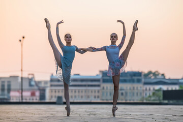 Obraz na płótnie Canvas Two young ballerinas dancing in pointe shoes in city against the backdrop of sunset sky