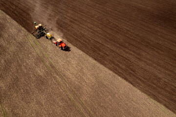Farmer on tractor cultivates and plows plough land of field for planting cereals . Aerial top view...