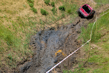 An open pit with slopes and off-road terrain for competition driving through the swamp on off-road vehicles with increased cross-country ability, dirty red car on mud landscape.