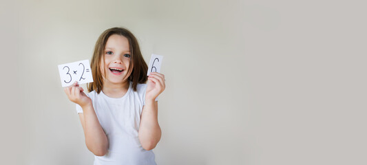 cute kid girl in mustard dress learns the multiplication table on beige background, child with an example sheet and numbers in his hands