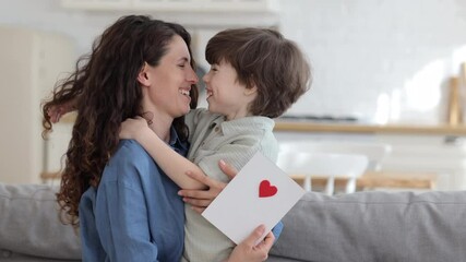 Cute preschool son congratulating young mom with mother day, valentine day or birthday give mommy handmade postcard with red heart. Loving mum and kid cuddling embrace cheerful to family holiday event