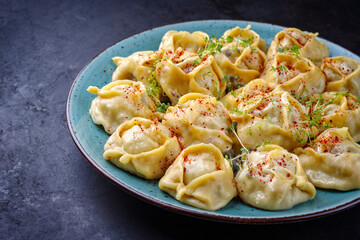 Traditional steamed Kazakh manti garnished with mincemeat and sumah served as close-up on a Nordic design plate with copy space left