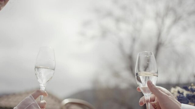Close up side view of groom and bride hands clinking glasses with wine during their wedding. Action. Concept of celebration and starting family.