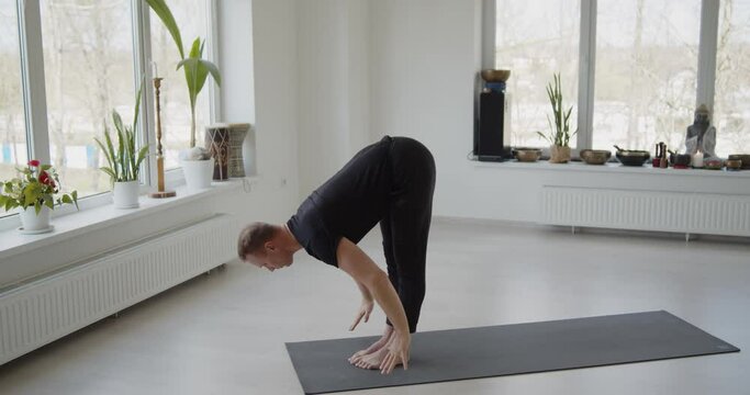 Professional trainer practices flow yoga in private class. Adult man makes yoga asanas on a mat in white bright studio. Fitness, healthy lifestyle and wellness concept.
