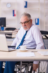 Old male employee in wheel-chair sitting in the office