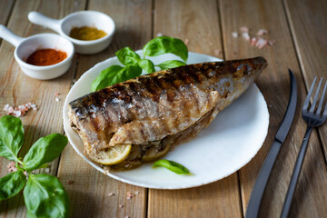 Fish lunch: grilled mackerel on a white plate on a wooden table.